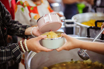 The concept of giving: Homeless people reach out to free volunteer meals from volunteers: help feed the hungry in society.