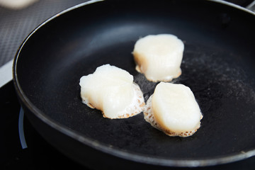  raw scallops in a black pan, fried in oil, cooking, seafood