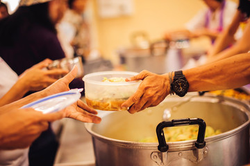 The concept of giving: Homeless people reach out to free volunteer meals from volunteers: help feed the hungry in society.