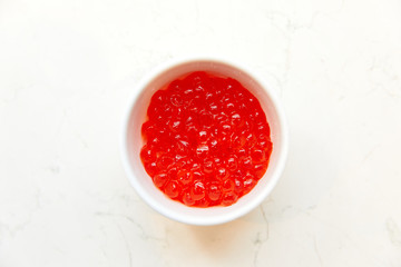 large Red caviar, in a white saucer, standing on a table on a white background