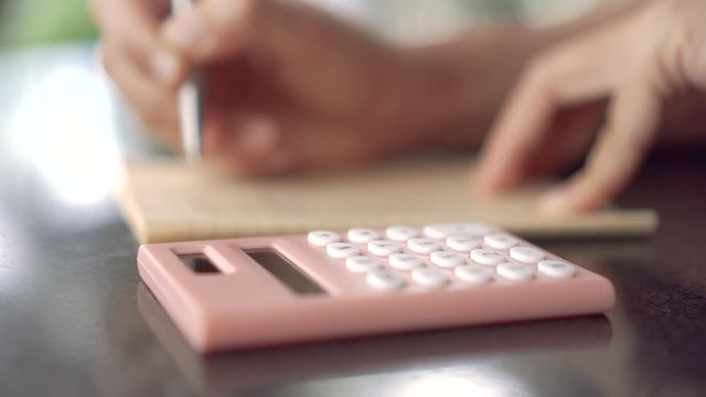 4K video copy space of  man hand writing down in white notebook and calculate with calculator with bokeh light in cafe background.