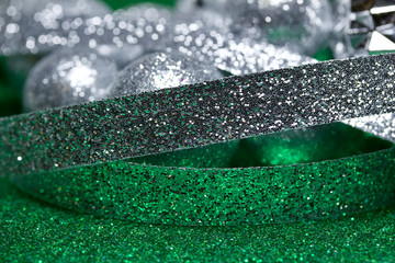 Macro abstract view of sparkling silver holiday baubles and ribbons on green glitter background with bokeh