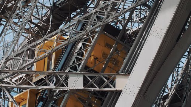 Close-up tracking shot of funicular elevator moving upwards among the steel structure bars of Eiffel Tower in Paris.