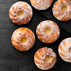 Mini bundt cakes or muffins with icing sugar on black wooden background.