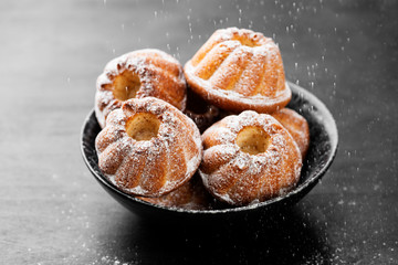 Mini bundt cakes or muffins with icing sugar on black wooden background.