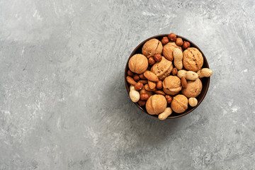 Bowl of various nuts, walnuts, almonds, hazelnuts and peanuts on gray background. Top view, copy...