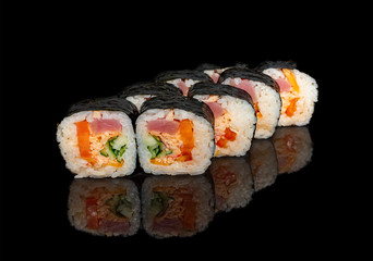 sushi and rolls with different fillings on a black background with reflection