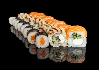 sushi and rolls with different fillings on a black background with reflection