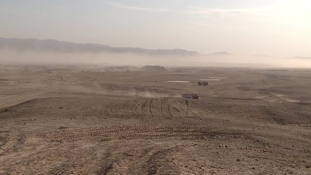 Military cargo convoy rides fast in desert sand dunes, leaving behind a massive trail of dust, military operation. The convoy group is moving in formation to meet the combat attack