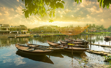 Wooden boats on the Thu Bon River in Hoi An Ancient Town, Vietnam. Yellow old houses on waterfront reflected in river. Vietnam