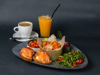 Hearty breakfast - fried potatoes, beans, two sandwiches with fetax cheese and salmon, rucola and tomato salad with pesto sauce. On a dark background
