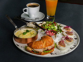 Hearty breakfast - corn porridge, croissant with sliced chicken, rucola, tomato and cheese salad with pesto sauce, boiled chicken eggs with chicken pate