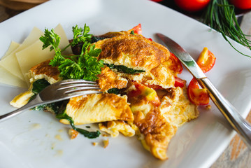 Traditional omelet with vegetables, spinach, tomatoes and herbs on a wooden table in a restaurant.