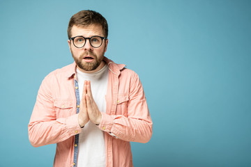 Bearded man is bewildered, he folded hands in a plea for help and looks at the camera. Copy space....