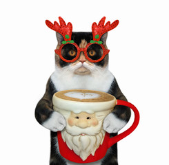 The multi-colored cat in a red glasses is drinking coffee from a big red Christmas cup. White background. Isolated