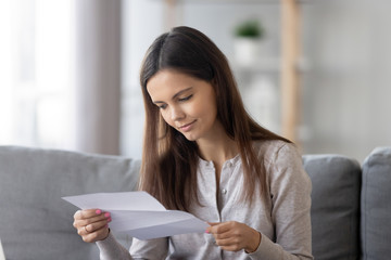 Young woman sit on couch reading paper letter
