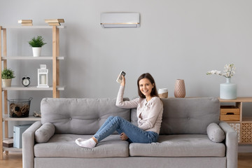 Smiling girl relax on couch turn on air conditioner