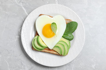 Tasty breakfast with heart shaped fried egg on grey table, top view