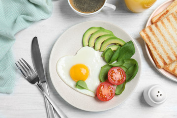 Tasty breakfast with heart shaped fried egg served on white wooden table, flat lay