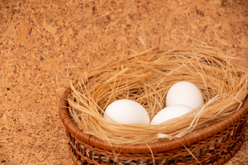 White chicken eggs are in a wicker basket with straw on a cork background. Easter card. Flat lay. Copy space.