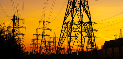 Electricity pylons bearing the power supply across a rural landscape during sunset. Selective focus. - obrazy, fototapety, plakaty