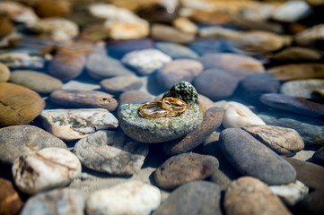 Fototapeta premium wedding rings lie on the sea rock on water background. Wedding details concept. CLoseup