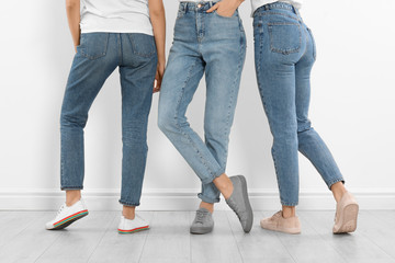 Group of young women in stylish jeans near white wall, closeup