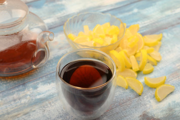Marmalade lemon slices, a glass of black tea and a teapot with brewed tea on a wooden background. Sweet dessert. Close up.