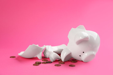 Broken piggy bank with coins on pink background