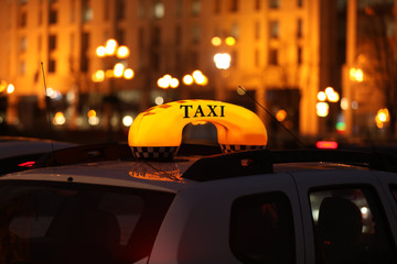 Taxi car with yellow checkered sign on city street in evening, closeup