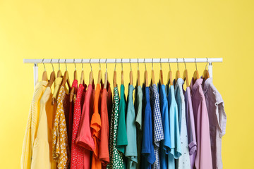 Bright clothes hanging on rack against yellow background. Rainbow colors
