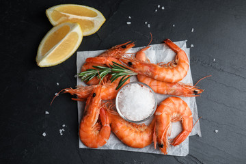 Delicious cooked shrimps with rosemary, lemon and salt on black table, flat lay