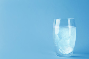 Glass of water with effervescent tablet on light grey background, space for text