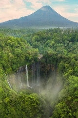 Obraz premium View from above, stunning aerial view of the Tumpak Sewu Waterfalls also known as Coban Sewu with clouds raising from the canyon. Semeru volcano in the distance, Malang Regency,East Java, Indonesia.
