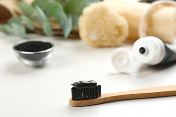 Bamboo toothbrush with charcoal paste on white table, closeup. Space for text