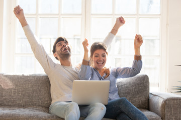 Happy young couple celebrate online victory, using laptop together