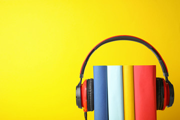 Books with modern headphones on yellow background. Space for text