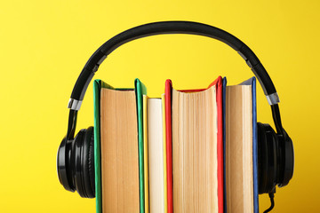 Books with modern headphones on yellow background, closeup
