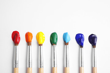 Brushes with bright paints on white background, flat lay. Rainbow colors