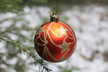 Red glass ball with golden patterns, Christmas tree toy on a Christmas tree branch in a winter forest.