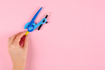 Hand with blue stationery compass for kids on pink background.