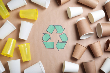 Recycling symbol, plastic and paper cups on beige background, flat lay