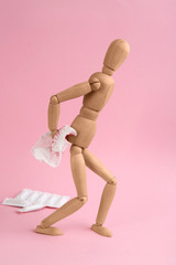 Wooden human figure and sheet of toilet paper with blood on pink background. Hemorrhoid problems