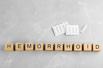 Wooden cubes with word HEMORRHOID and suppositories on grey marble table, flat lay