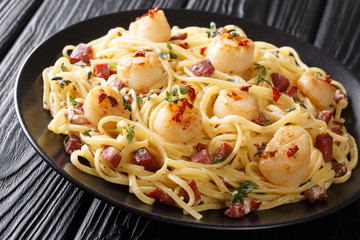 Serving of spaghetti with scallops and bacon in a creamy cheese sauce close-up in a plate on the table. horizontal
