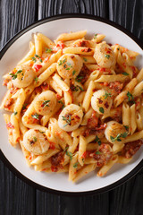 Penne pasta with scallops, tomatoes, herbs and spicy sauce close-up in a plate. Vertical top view