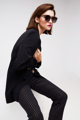 High fashion portrait of young elegant woman. Sunglasses, black jacket, pants.