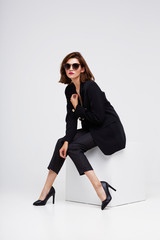 High fashion portrait of young elegant woman. Sunglasses, black jacket, pants.