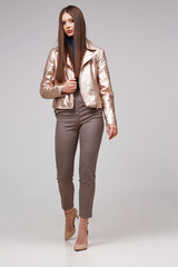 Fashion model in golden leather jacket posing in studio.