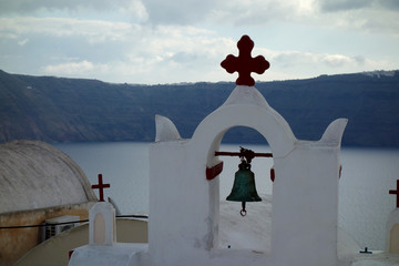 A cross with a bell construction in Santorini with the sea at the background
